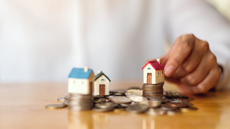 a woman's hand putting house model on pile of coins for saving money concept