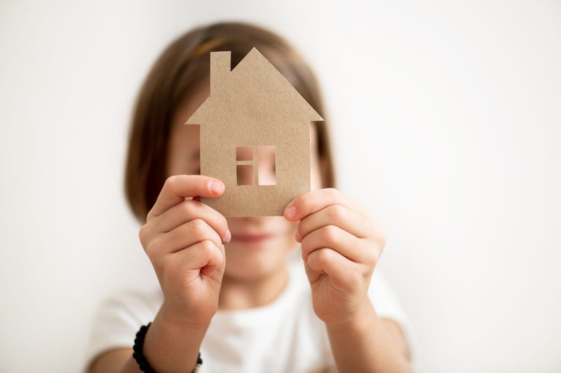 Little girl holding paper house in front of her face. 