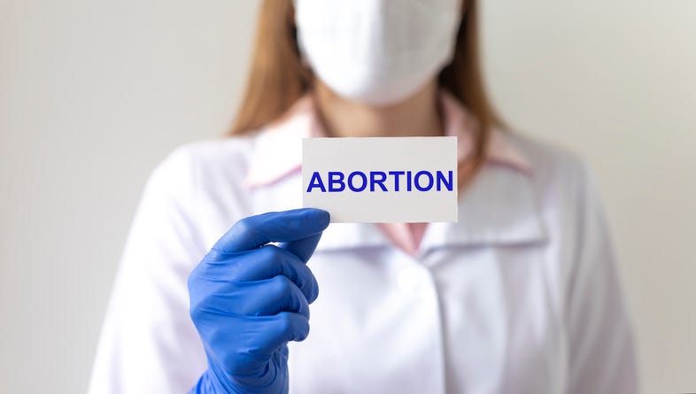Doctor woman in protective gloves holds a paper with text abortion