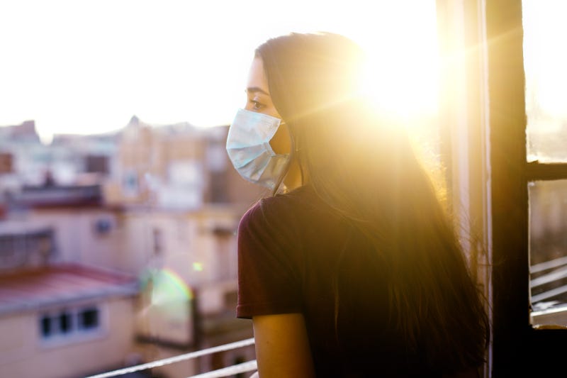 masked woman looking out her window