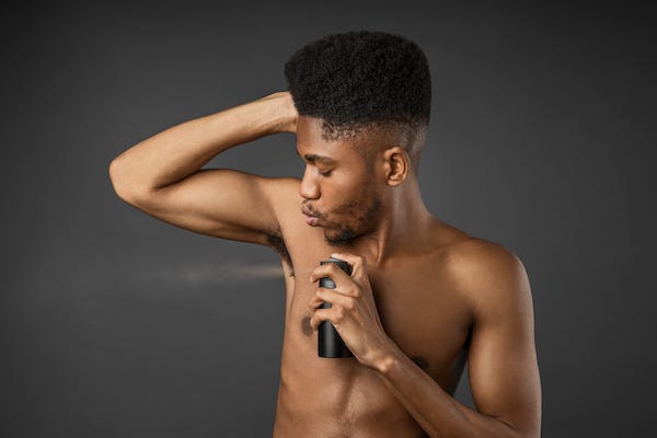 Man spraying body spray under arms