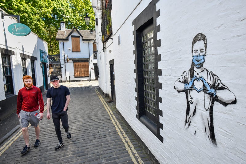 Members of the public walk past graffiti in the West End during the coronavirus lockdown on May 6, 2020 in Glasgow, Scotland. on May 06, 2020 in Glasgow. The country continued quarantine measures intended to curb the spread of Covid-19, but the infection rate is falling, and government officials are discussing the terms under which it would ease the lockdown. 