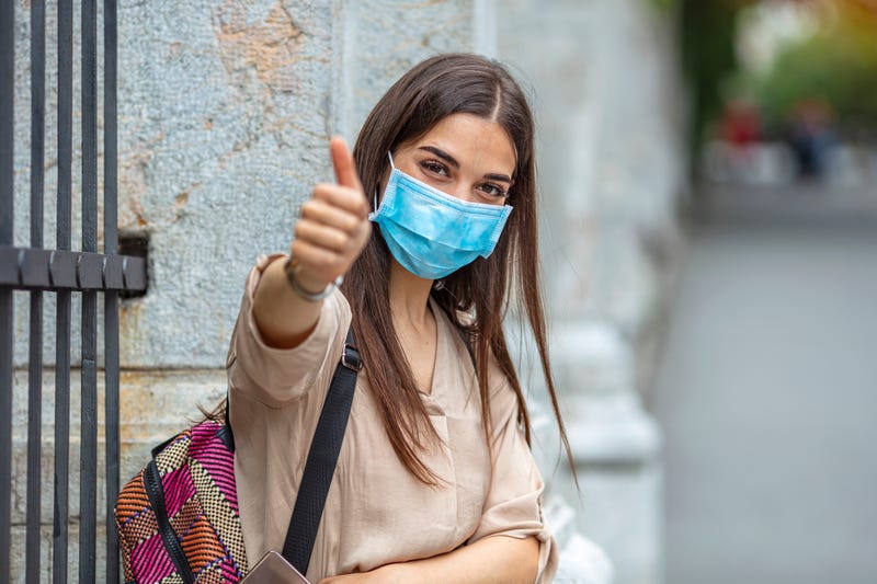 Beautiful caucasian young woman with disposable face mask. Protection versus viruses and infection. Woman showing thumb up.