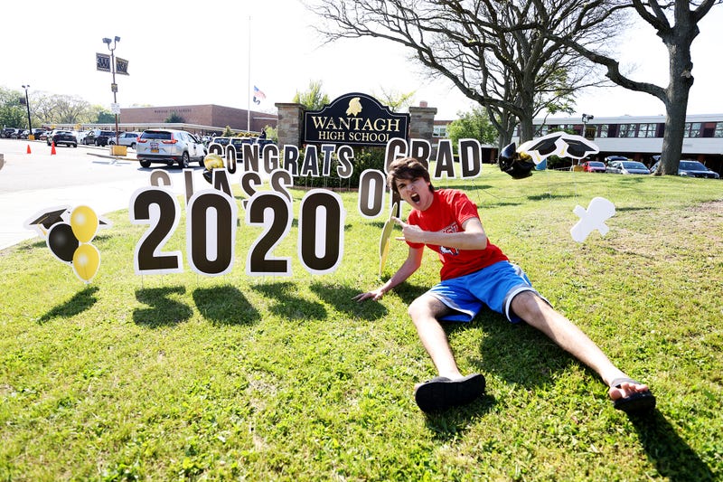 John Sileo, Wantagh High School Class of 2020 Co-President poses in front of a sign on the grass as graduating Seniors from Wantagh High School drive by the front of the school and their teachers cheer for them on May 15, 2020 in Wantagh, New York.