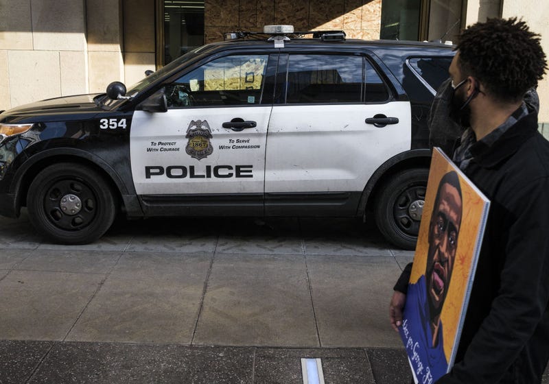 A man carrying a portrait of George Floyd looks on at a police cruiser as demonstrators march in honor of George Floyd on March 7, 2021 in Minneapolis, Minnesota.