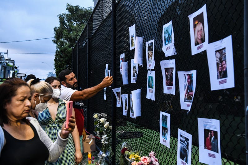People look at pictures of missing residents of the partially collapsed building at a makeshift memorial in Surfside, north of Miami Beach, on June 25, 2021. - Four people were confirmed dead and 159 unaccounted for Friday following the collapse of an oceanfront apartment building near Miami Beach, as rescue teams scoured a mountain of rubble in a desperate search for survivors