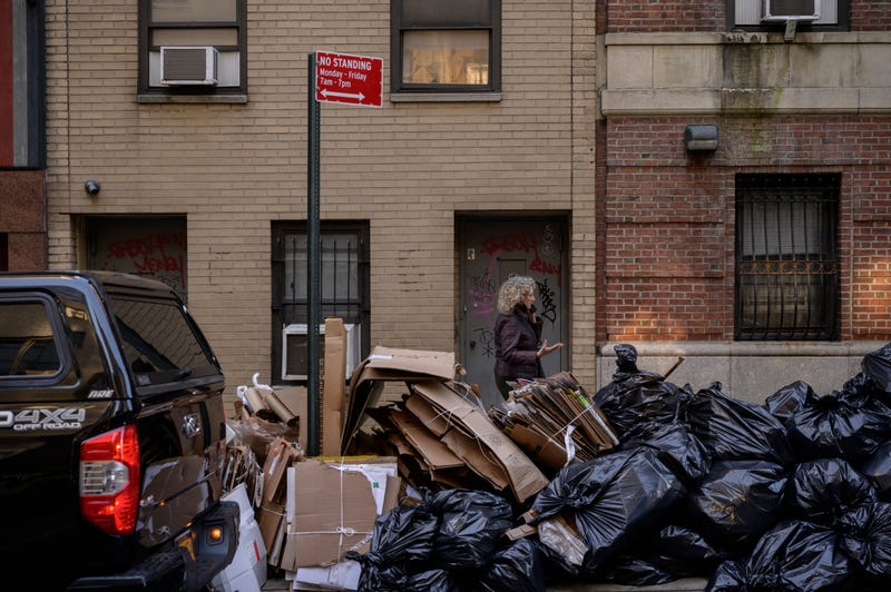 Pedestrians pass by trash bags piled on a street in Manhattan