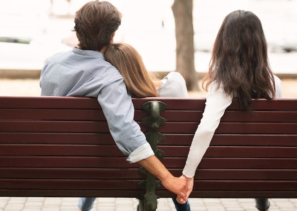 Man holding hands with another woman while cuddling with girlfriend on a bench
