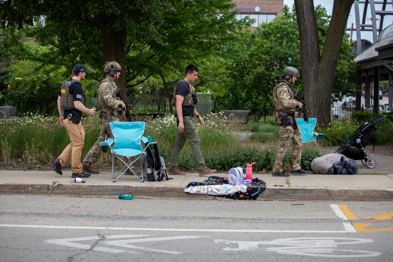 Authorities walk the scene of a Highland Park mass shooting