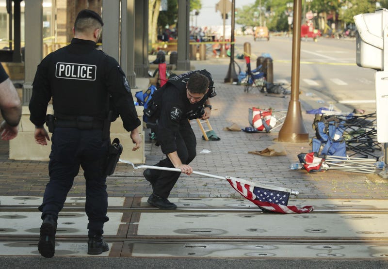 A police officer picks up a water-logged American flag, Tuesday, July 5, 2022, left behind after Monday's mass shooting in Highland Park.