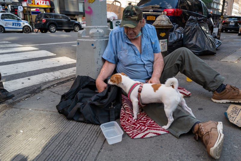 John, who is homeless, sits with his dog Daisy on a Manhattan street during a heat wave on July 22, 2022 in New York City.