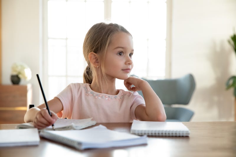 Child sitting at a table writing and thinking