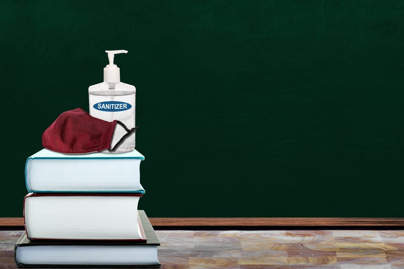 Education concept of New Normal in schools during Covid-19 pandemic with classroom setting of books, hand sanitizer and cloth face mask on table. Back to school measures to contain coronavirus outbreak with copy space on chalkboard.