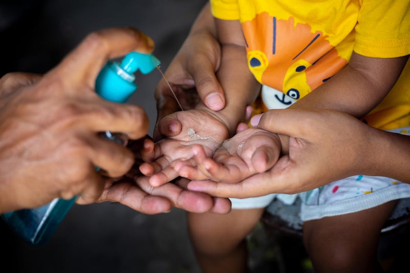child learning to use hand sanitizer to prevent the spread of COVID-19