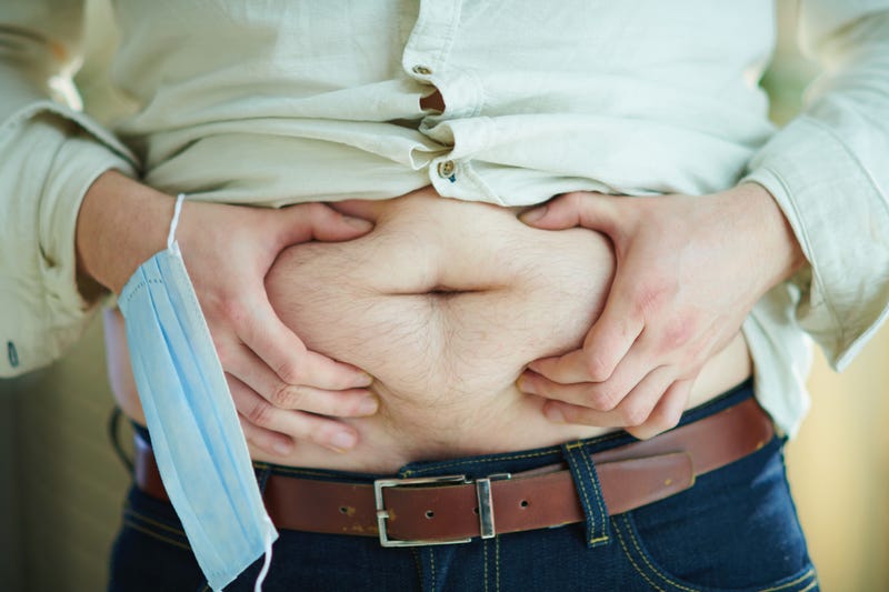 Male with medical mask checking body fat by grabbing stomach.