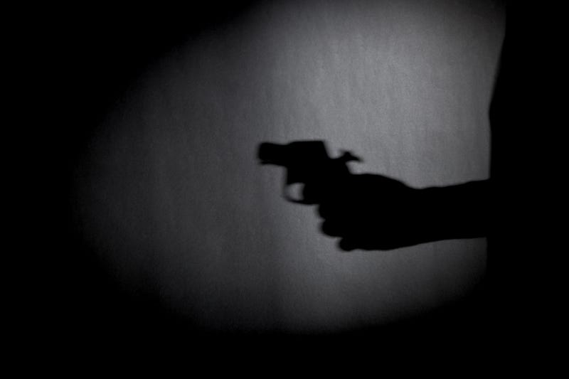 Stock image of a hand holding a gun in shadow. 