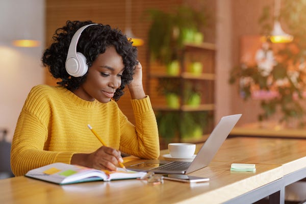 Young woman doing schoolwork while listening to music on headphones