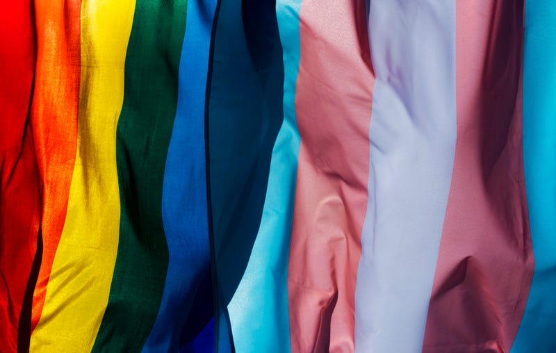 closeup of a gay pride flag and a transgender pride flag waving on the blue sky, moved by the wind