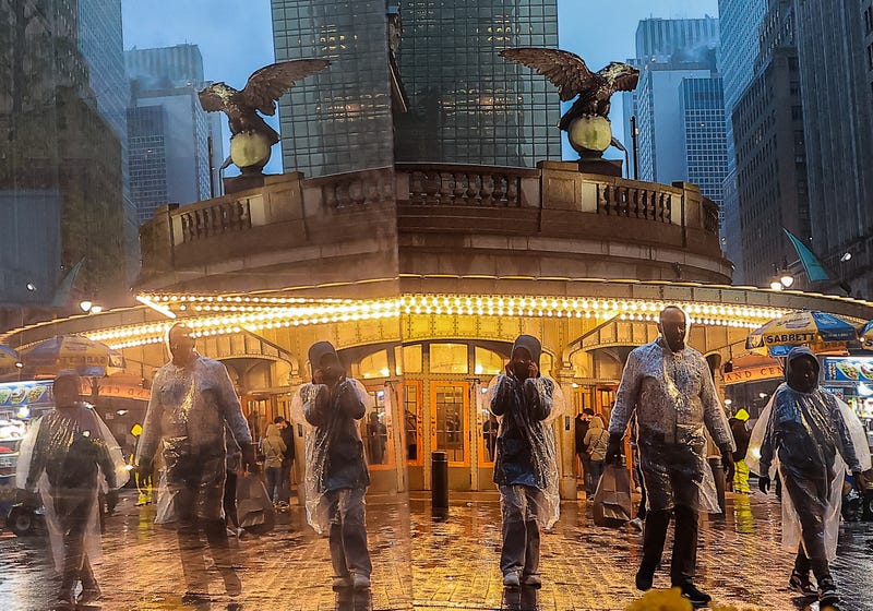 People walk on the street with their raincoats as their reflection is seen on a building in New York, United States on April 30, 2023