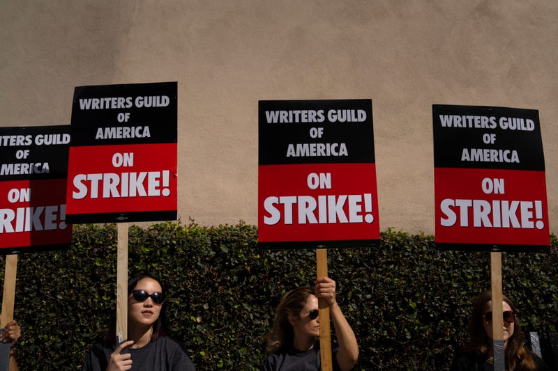 picketers holding signs that say writers guild of america on strike