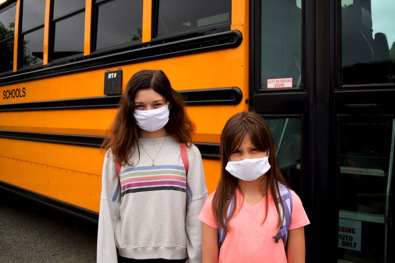 Two school children are wearing facemasks to protect themselves while standing by a school bus. For healthcare, medical, education, and coronavirus concepts.