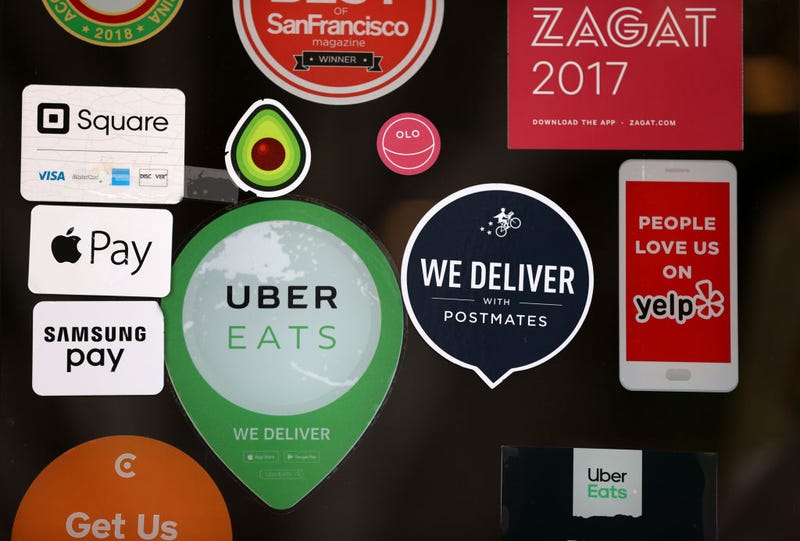 A Postmates sticker is displayed next to an Uber Eats sticker on the window of a restaurant on July 06, 2020 in San Francisco, California.
