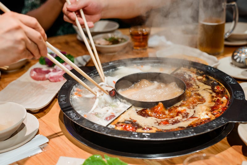 Eating a hot pot dish with chopsticks. Close up shot of appetizing food and traditional serving in Chinese restaurant.