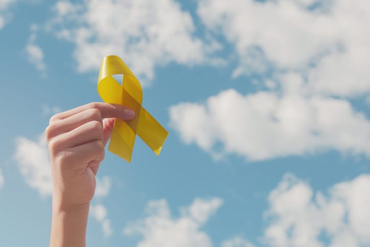 Hands holding yellow gold ribbon over blue sky