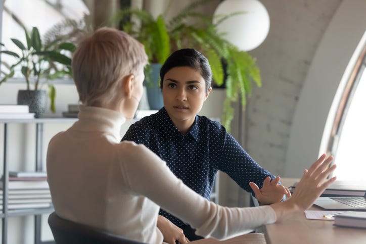 ndian and caucasian businesswomen negotiating sit at desk in office
