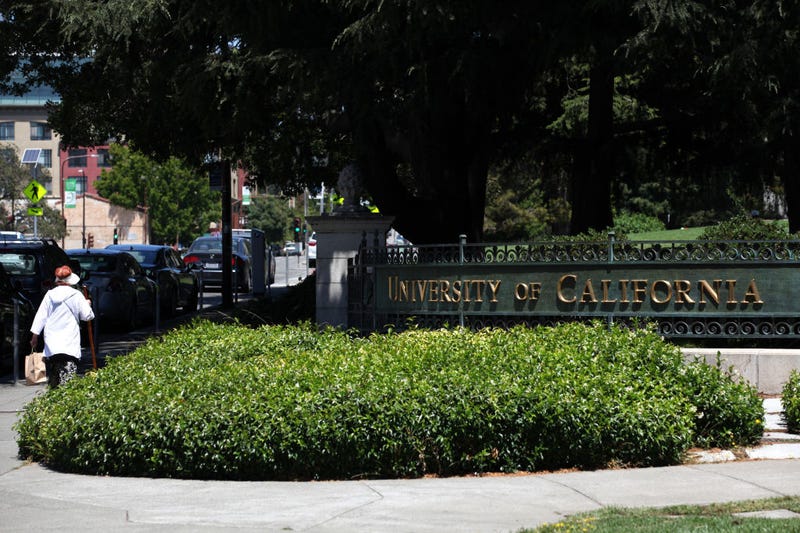 A pedestrian walks by a sign in front of the U.C. Berkeley campus.