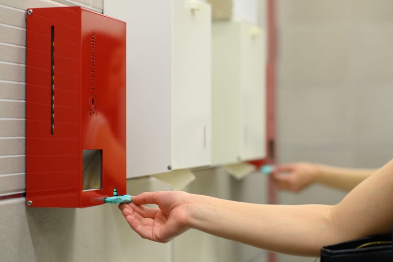 A woman uses a tampon and pad dispenser in a women's restroom
