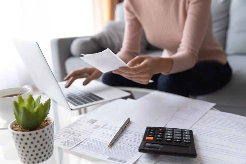 File photo of woman sitting at laptop with a calculator and bills.