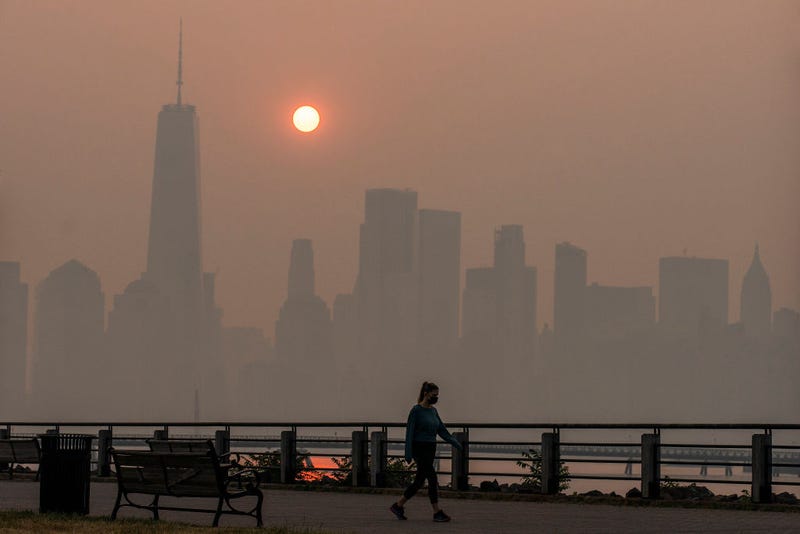 A woman walks as the sun rises behind the One World Trade Center and the New York skyline, while the smoke from Canada wildfires covers the Manhattan borough as it is seen from the Liberty State Park on June 8, 2023 in New Jersey. 