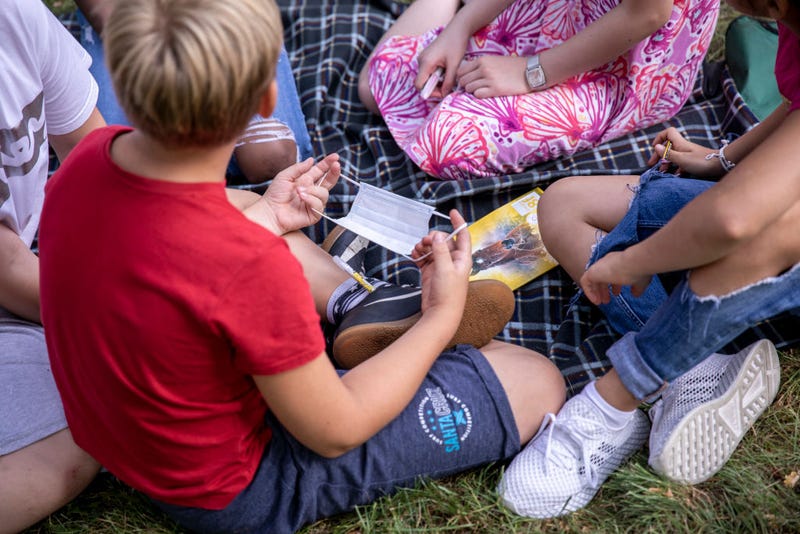 Child holds protective mask as he and his schoolmates learn outside during first day of classes of the new school year at the GuthsMuths elementary school.
