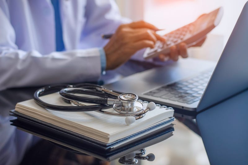 Female doctor or practitioner using calculator and work on laptop computer with medical stethoscope and notebook on the desk at clinic or hospital