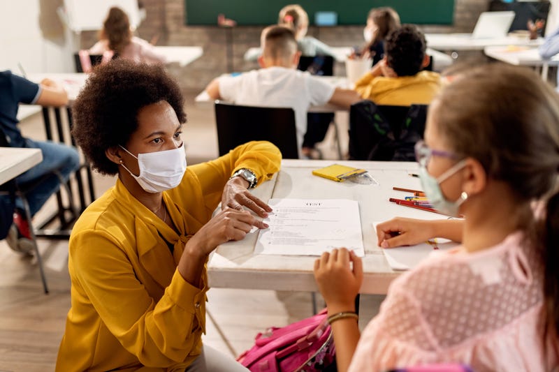 Teacher with a face mask explaining exam results to an elementary student in the classroom.
