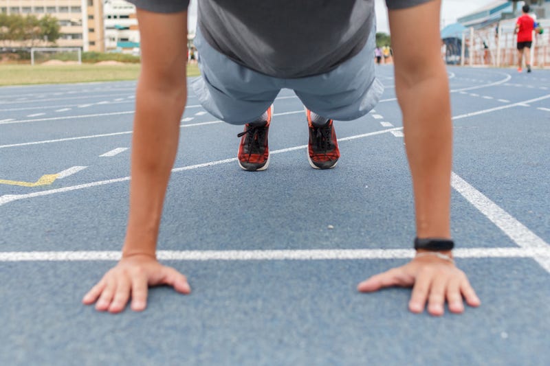 Sport man doing push ups exercise on the blue running track in stadium