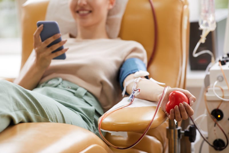 lose-up of young woman lying on the couch with mobile phone while donating blood at the laboratory