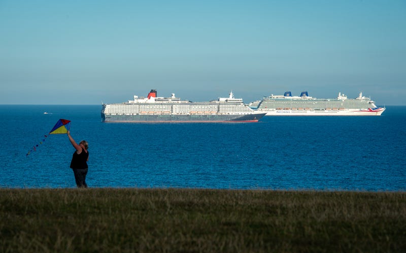 A woman flies a kite with the backdrop of cruise ships (l-r), Queen Elizabeth and Britannia anchored in the English Channel off the Dorset coast in Weymouth, England.