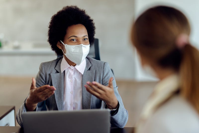 Two women with masks speaking to one another in a professional setting
