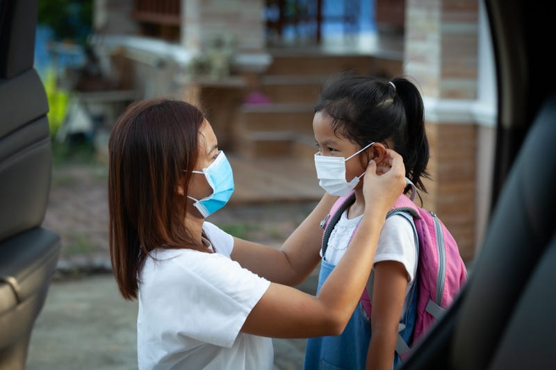 A mother putting a mask on her daughter.