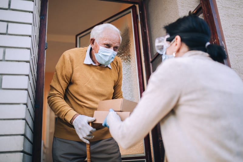 female volunteer in mask gives an elderly man boxes with food near his house