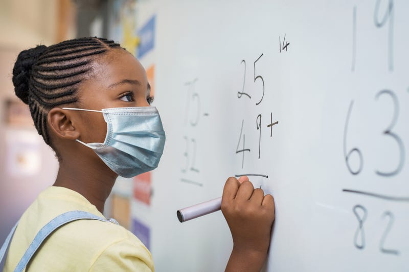 Black schoolgirl solving addition sum on white board during Covid-19 pandemic.