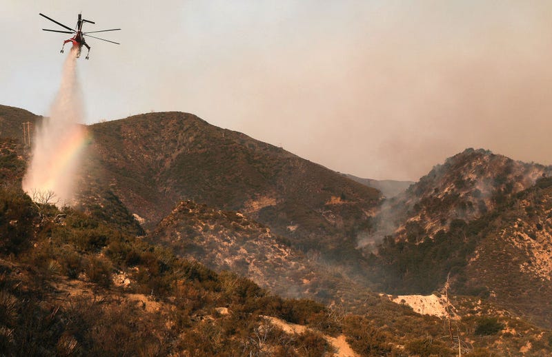 FILE - A firefighting helicopter makes a water drop, as a rainbow appears in the mist, during the Bobcat Fire in the Angeles National Forest on September 23, 2020 near Pasadena, Calif.