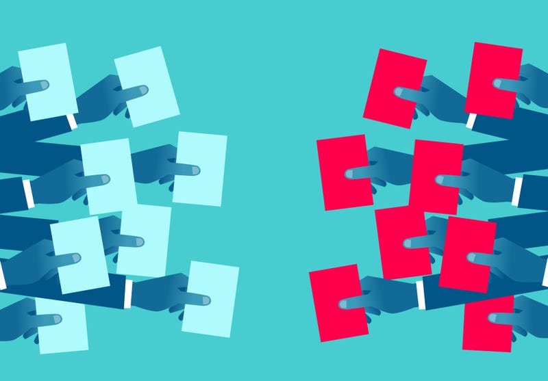 Two groups of hands holding ballots of different colors 