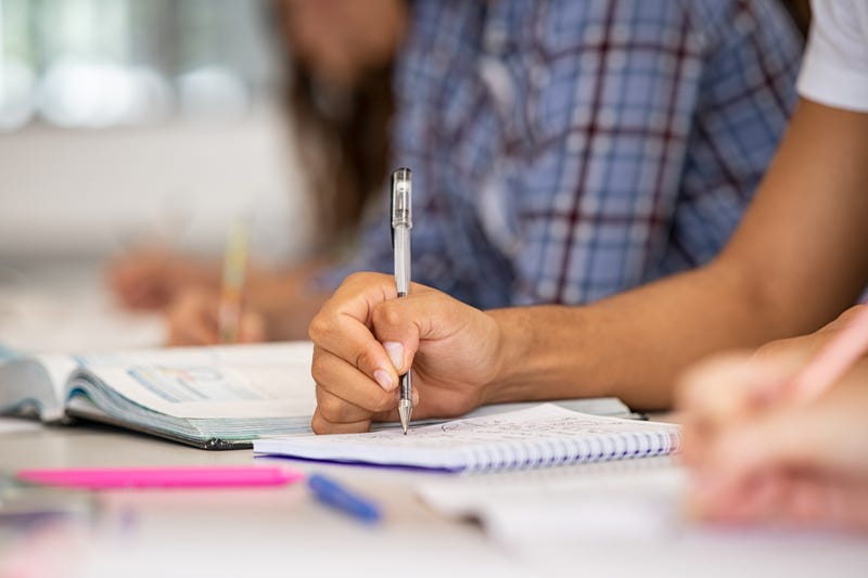 File image - Close up of a student's hand on the table in a classroom taking notes. Two students at a charter school in Temecula were recently forced off the campus after refusing to wear a mask due to religious reasons.