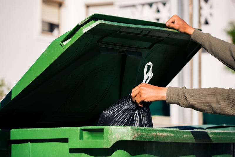 person throwing trash bag in green trash bin