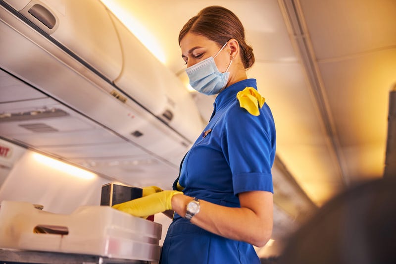 Waist-up photo of a flight attendant in a face mask and yellow gloves distributing meals to the passengers