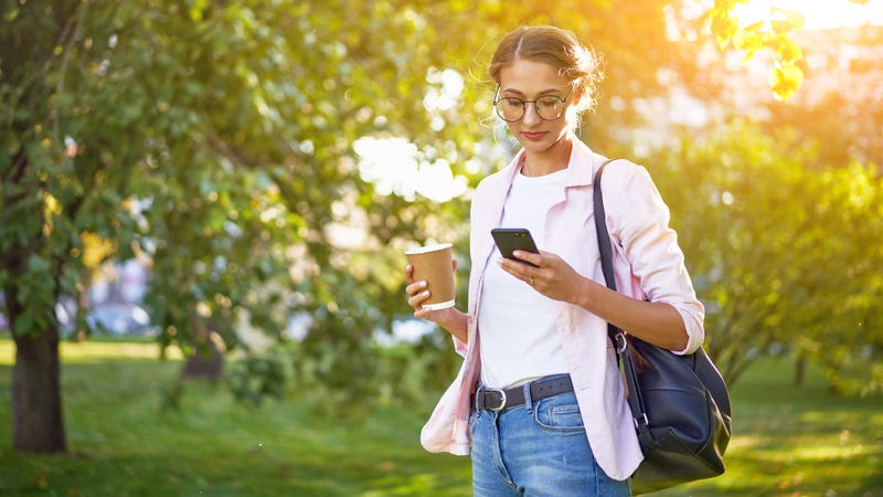 Woman reading news on cell phone outside while holding coffee