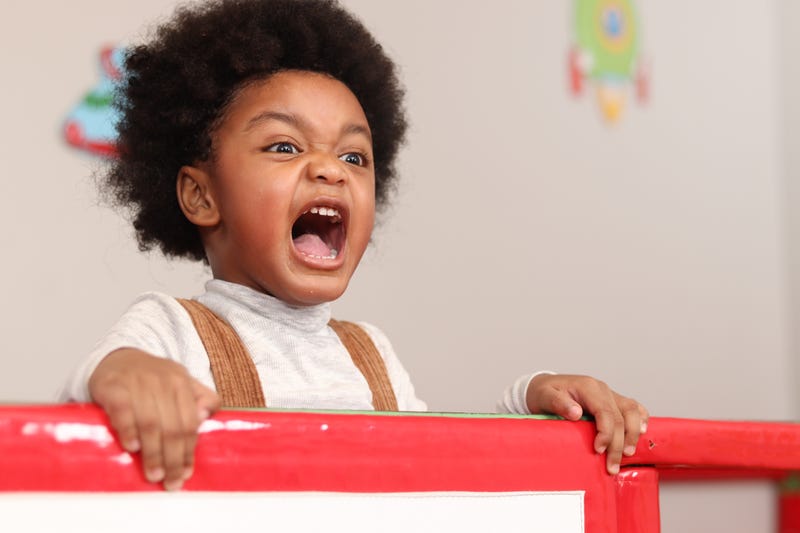 boy with curly hair shouting while playing at the playground, kid having fun on playground.